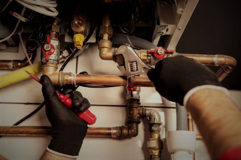 Zbliżenie na dłonie instalatora i serwisanta firmy Qborg, pracującego z kluczem i śrubokrętem na elementami instalacji gazowej